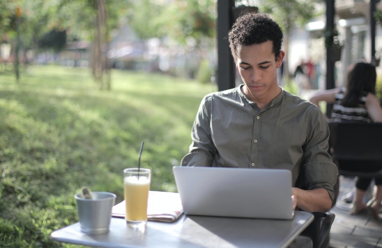 A man sitting at an outdoor table with a laptop.